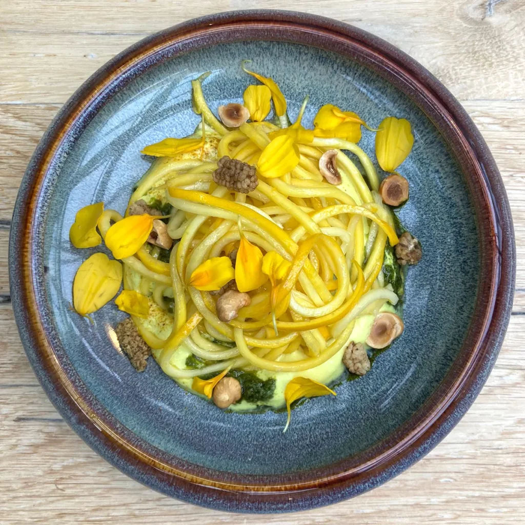 Spaghetti van gele courgette geserveerd met pesto hazelnoten en courgette bloemen